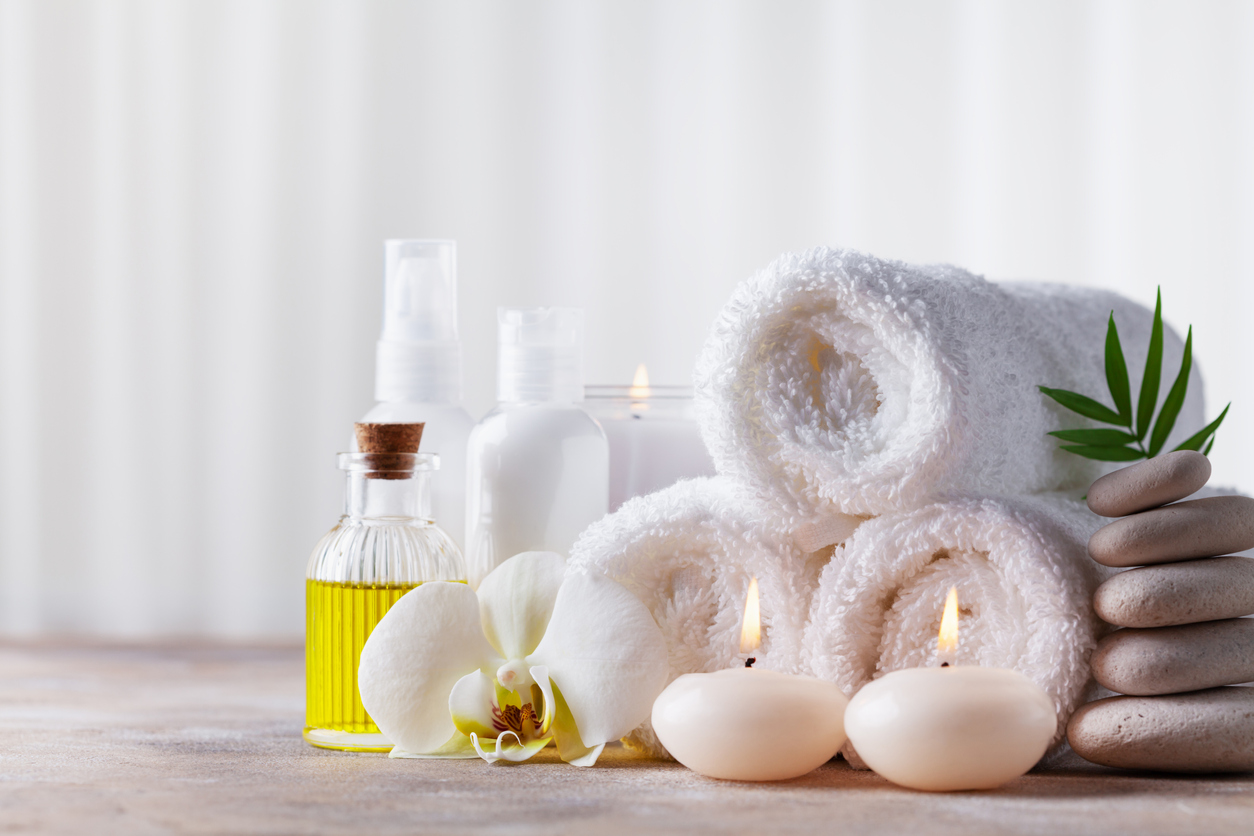 Spa, beauty treatment and wellness background with massage pebbles, orchid flowers, towels, cosmetic products and burning candles.